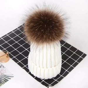 Detailed view of a white cable-knit beanie with a fluffy brown faux fur pom-pom on top