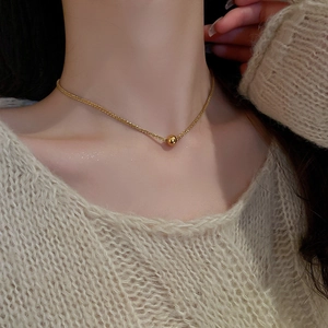 Close-up of a minimalist golden bead pendant on a woven titanium steel chain for women