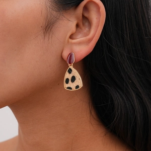 Close-up of model wearing gold earrings with brown oval and leopard print triangle pendants