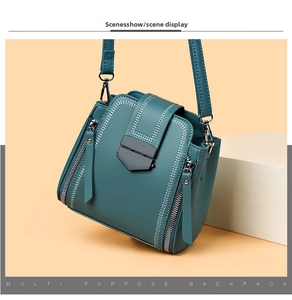 Detail view of teal leather handbag featuring silver stitching and dark metal shield buckle