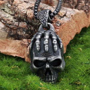 Detail of gothic silver skull pendant with skeletal hand on rustic moss background