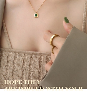 Detail of model wearing a gold bead chain with green zircon pendant and wavy ring