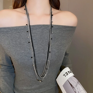 Detail shot of multilayered silver chain and black glass beads on a grey knit top