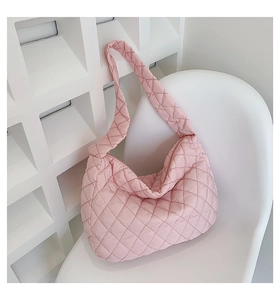 Detailed view of pink quilted tote bag with knot strap on a white chair background