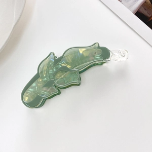 Detailed top view of a green iridescent acetate leaf-shaped banana hair clip on white surface