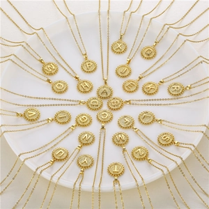 Close-up of gold initial round pendant necklaces with engraved letters on a white plate