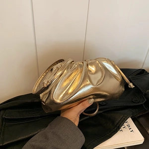 Metallic gold pleated cloud clutch bag with top handle shown held against dark leather