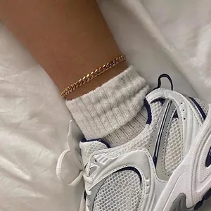Bracelet de cheville gourmette en acier inoxydable doré porté sur des chaussettes blanches