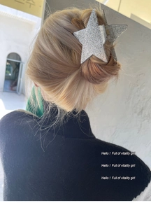 Star-shaped hair claw clip with silver glitter finish worn on wavy blonde hair