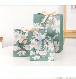 Three green floral gift bags in various sizes with woven handles and elegant ribbon bows