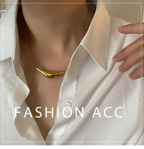 Gros plan d'un collier doré avec pendentif incurvé porté sur une chemise blanche