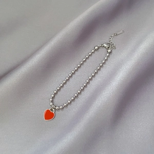 Detail shot of silver bead bracelet with red heart pendant on grey silk background