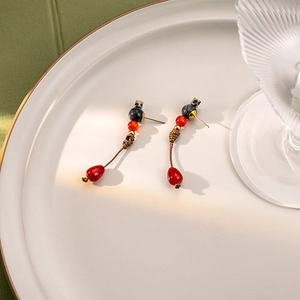 Close-up of red beaded teardrop earrings with gold accents on a white ceramic plate