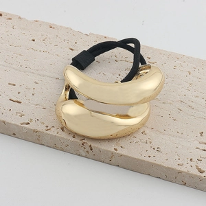 Detailed close-up of a polished gold liquid metal hair tie on a beige stone surface