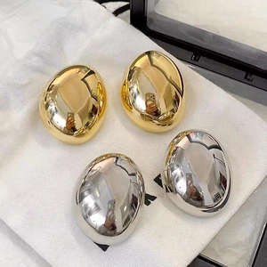 Macro detail of oval pebble earrings in polished gold and silver finishes on linen