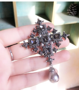 Macro shot of vintage cross brooch with dark gemstones and hanging grey water drop pearl