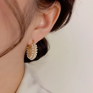 Elegant gold hoop earrings encrusted with rows of white pearls worn by a female model