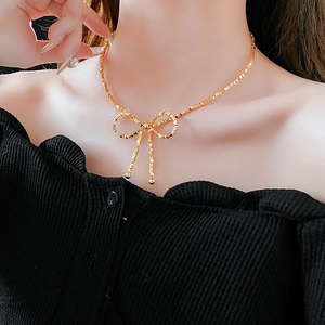 Detailed view of a gold-tone bow necklace with a block chain style on a female model