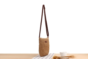Detailed view of handmade woven crossbody bag with slim brown leather straps on a table