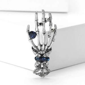 Detailed close-up of punk style skull hand brooch with blue and clear crystals