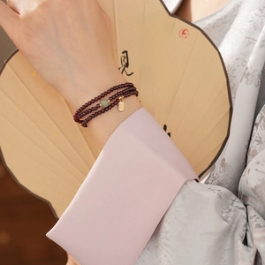 Detail of multi-layer garnet bead bracelet with gold charm and jade on traditional sleeve