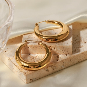 Detail of polished gold hoop earrings on stone base with elegant silk fabric backdrop