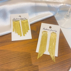 Detailed view of long gold fringe tassel earrings with zircon studs on silk backdrop
