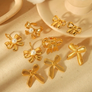 Golden bow jewelry set featuring elegant pearl rings and pendants on beige fabric