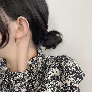 Close-up of woman wearing golden geometric square frame drop earrings in minimalist style