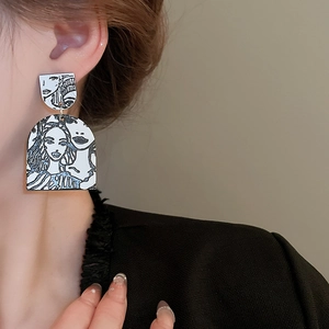 Close-up of minimalist abstract face earrings with black and white line art on a model