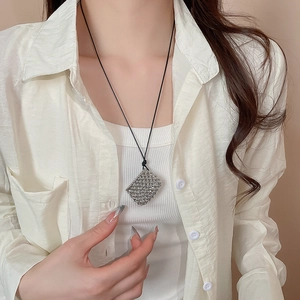Detail of silver mesh bag pendant on black wax cord worn with a minimalist cream outfit