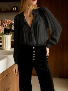 Detailed view of black pleated shirt with lace trim and gold buttoned high waist trousers
