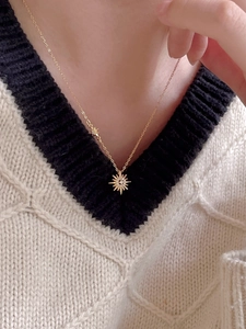 Close-up of golden starburst necklace with zircon pendant on a model wearing knitwear