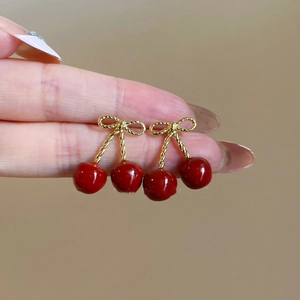 Detailed view of cherry pendant earrings with red glaze and golden bow accent