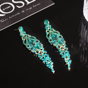 Elegant emerald teardrop tassel earrings with blue crystals on black reflective surface