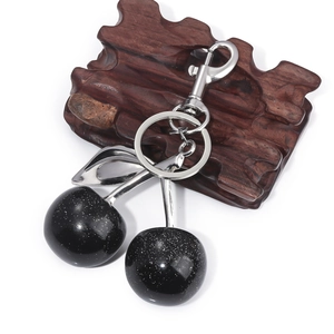 Detail of black glitter cherry keychain with silver leaves on a wood pedestal