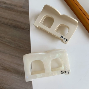 Detail view of acetate shark clips in beige and pearly white with Bry lettering