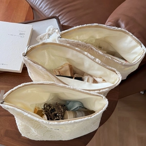 Lot de trois trousses à maquillage en dentelle beige disposées sur une table en bois