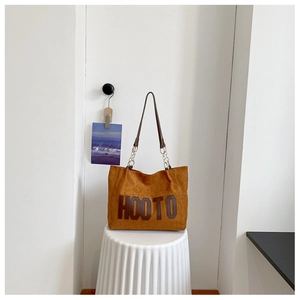 Close-up of caramel canvas tote bag with HOOTO letter print on a minimalist stool