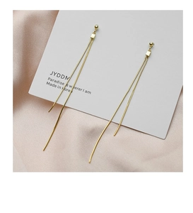 Detail showing elegant gold tassel drop earrings on white card over pink silk fabric