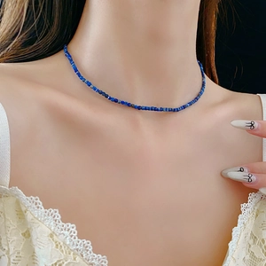Détail d'un collier ras du cou minimaliste en perles bleu foncé sur un modèle en dentelle