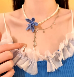 Detail view of a French style pearl necklace with a large blue beaded flower accent