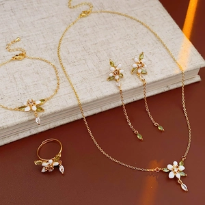 Set di gioielli smaltati con fiori bianchi e foglie verdi su un libro beige