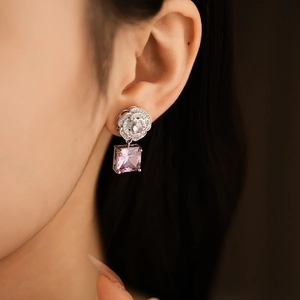 Close-up of silver floral stud earrings with square pink gemstone on woman ear