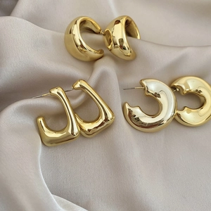 Detailed view of three pairs of chunky gold geometric earrings on beige satin fabric