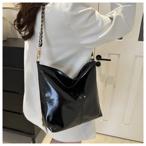 Detail of high-gloss patent leather tote bag with metal chain strap worn by a model