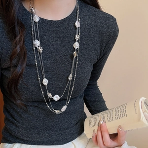 Detail of layered silver chain necklace with baroque pearls on a charcoal knit sweater