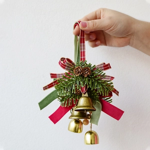 Christmas hanging ornament with golden bells pine cones and festive ribbons held by hand