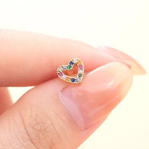 Close-up of golden heart earring with colorful zircon stones held by fingers