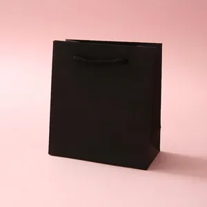 Minimalist matte black paper jewelry gift bag with woven rope handles on a lilac surface